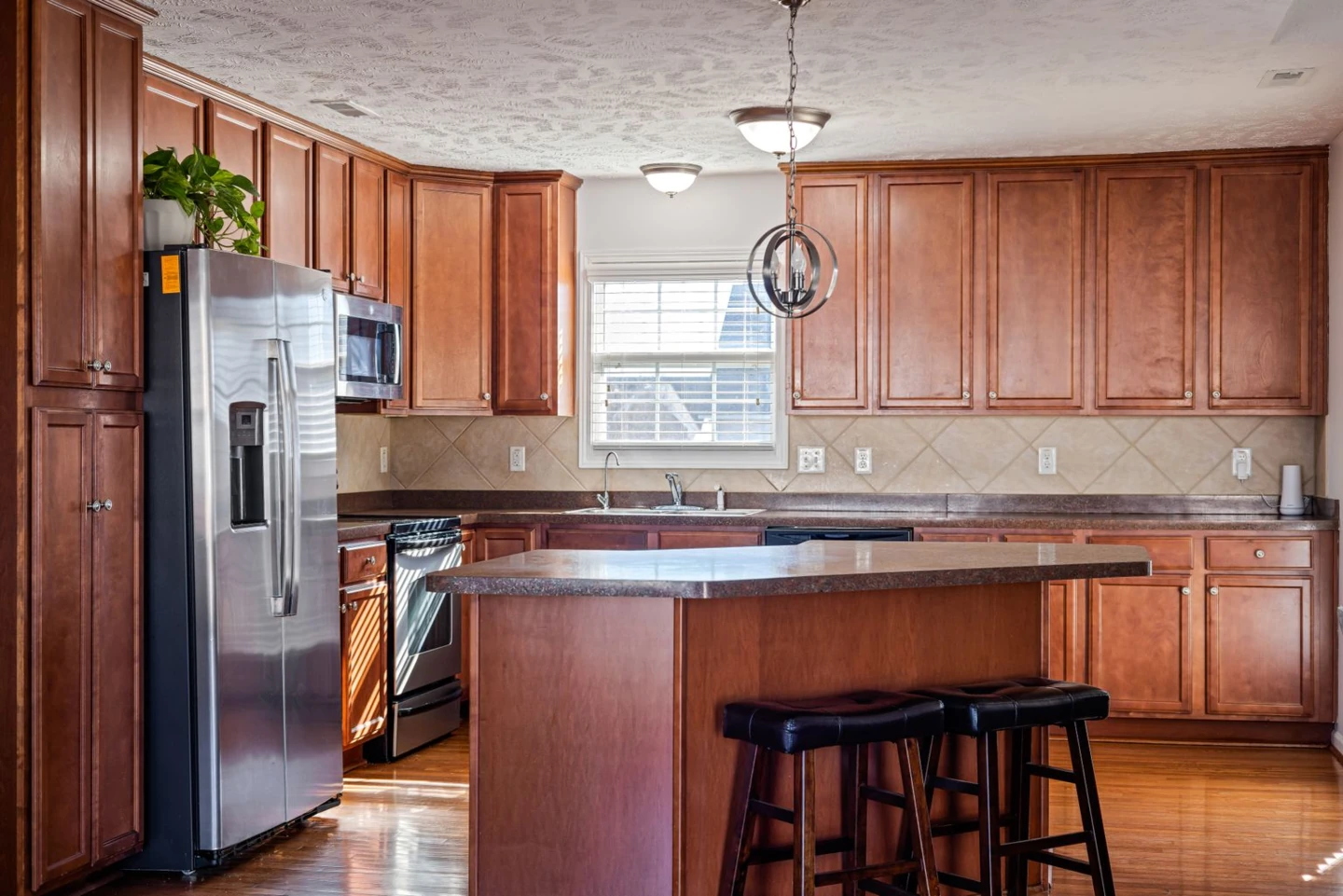 Original kitchen with brown wood cabinets, two stools and glossy wood flooring