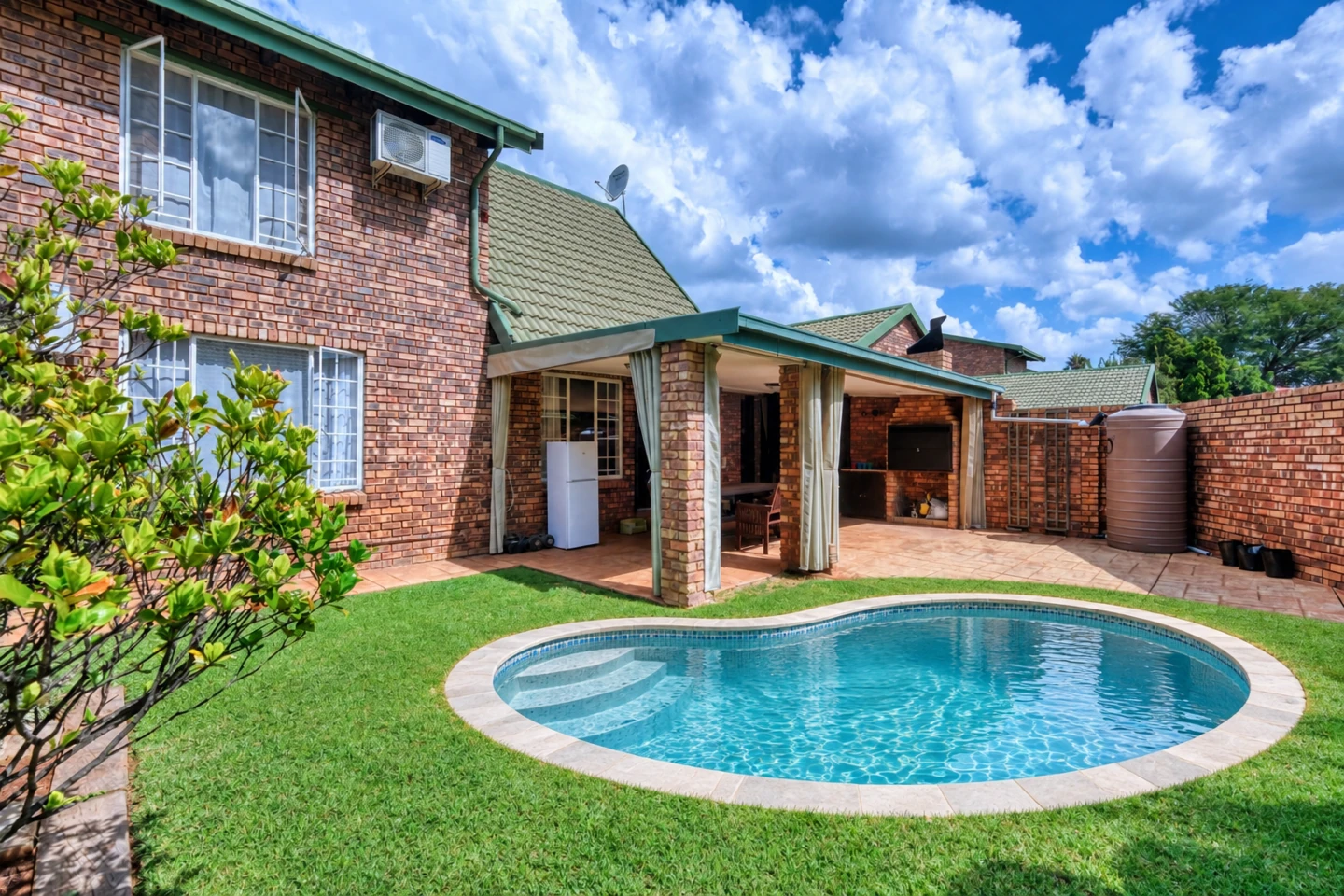 AI compact freeform swimming pool concept in the lawn outside the existing brick home