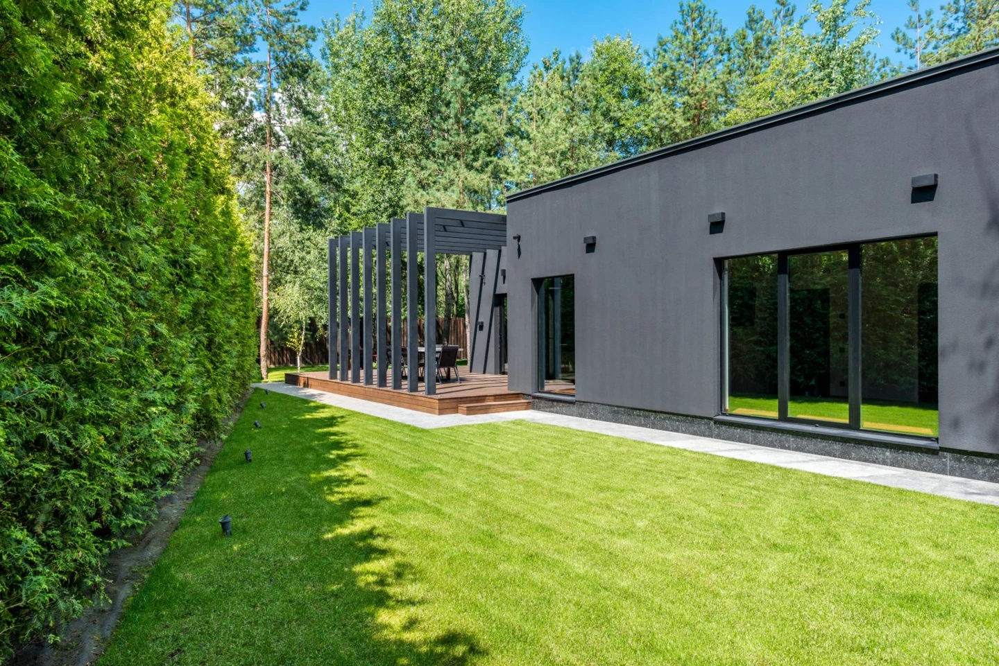Real narrow lawn between a tall hedge and a modern gray house